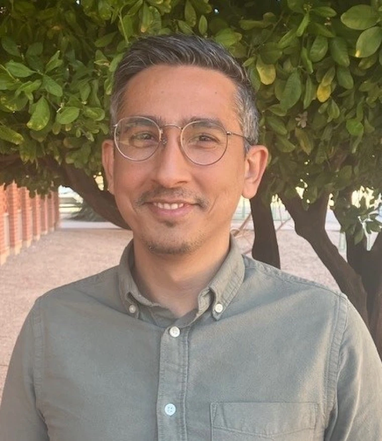 Postrait of individual with gray shirt and tree on background.
